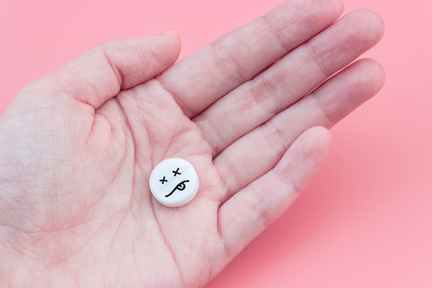 Comprimé avec emoji mort à la main sur fond rose Le concept de surdose de drogue