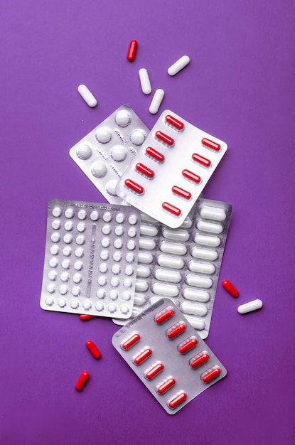 Photo comprimés pilules et capsules blanches rouges emballées et dispersées vue de dessus bannière verticale fond lilas