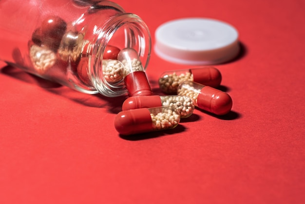 Comprimés rouges avec des granules blancs tombés d'un bocal en verre sur fond rouge Capsules médicinales
