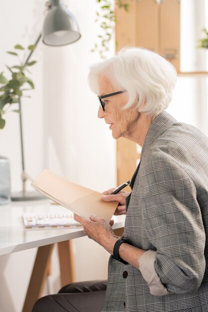 Comptable Principal En Tenues De Soirée Tenant Des Documents Financiers Tout En Jetant Un œil Aux Notes De Travail Au Bureau