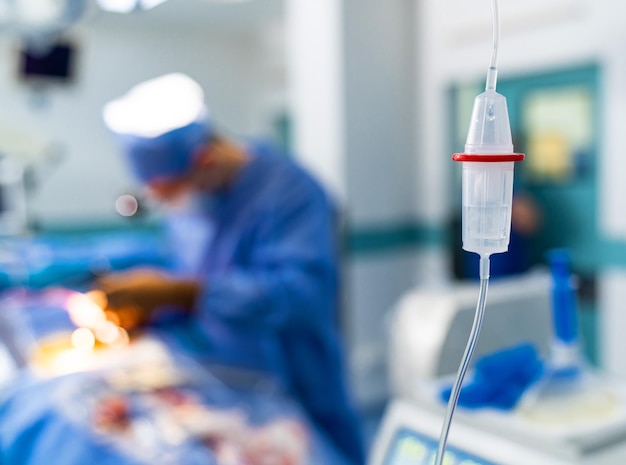 Un compte-gouttes avec un liquide physique Un neurochirurgien dans des lunettes de chirurgie spéciales assure l'opération Un médecin attentif et attentif dans la salle d'opération à l'arrière-plan