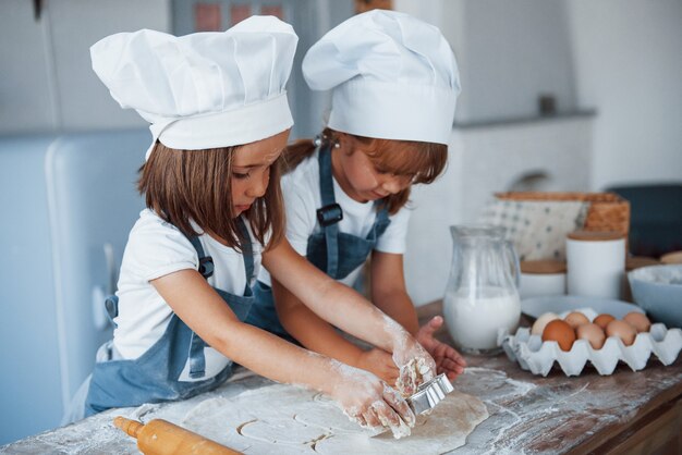 Photo concentration à la cuisson. enfants de la famille en uniforme de chef blanc préparant la nourriture dans la cuisine.