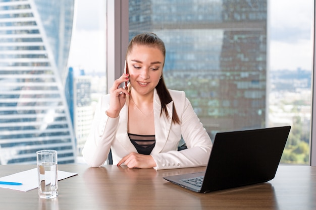 Concentré au travail. Confiant jeune femme en vêtements décontractés intelligents travaillant sur ordinateur portable tout en étant assis près de la fenêtre au bureau créatif