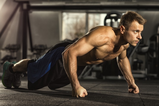 Concentré de beau jeune sportif fort faisant des pompes au gymnase