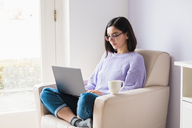 Concentré belle jeune femme dans des vêtements décontractés travaillant à domicile sur ordinateur