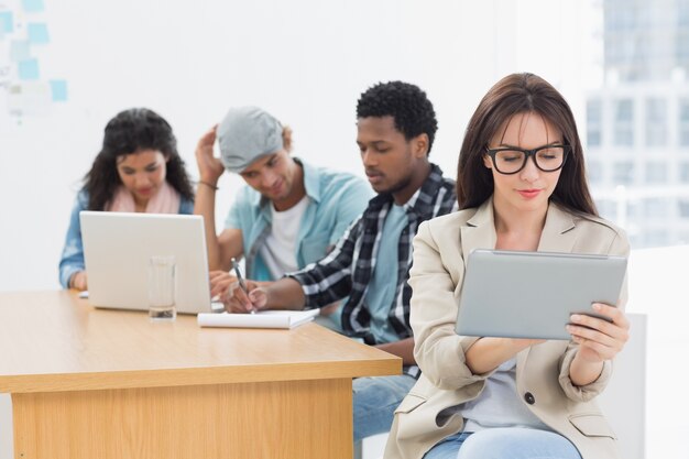 Concentré de femme à l&#39;aide de tablette numérique avec des collègues derrière le bureau