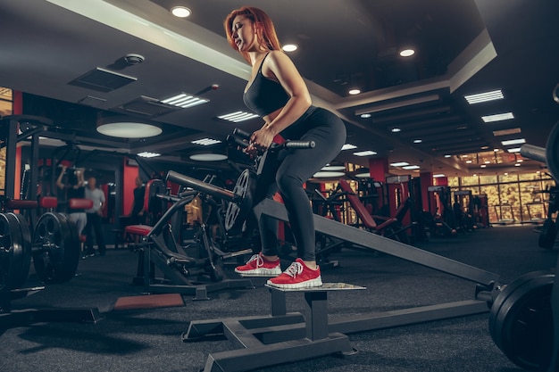 Concentré Jeune femme caucasienne musclée pratiquant dans une salle de sport avec équipement