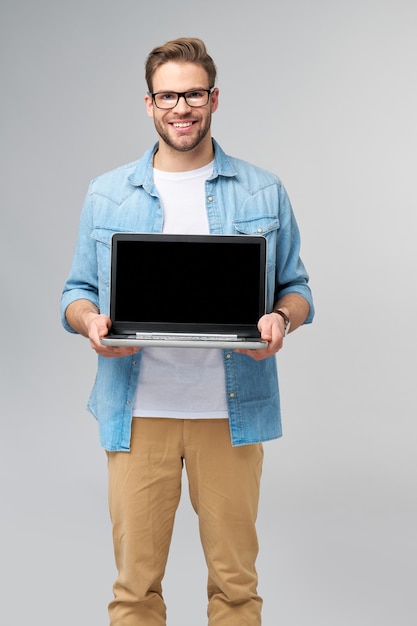 Concentré jeune homme barbu portant des lunettes habillé en chemise de jeans tenant un ordinateur portable