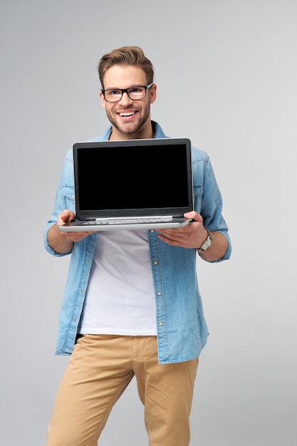 Concentré jeune homme barbu portant des lunettes habillé en chemise de jeans tenant un ordinateur portable