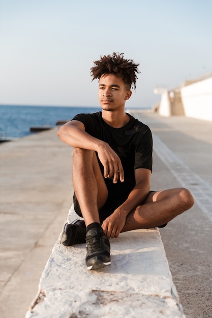 Concentré jeune sportif assis à l'extérieur sur la plage