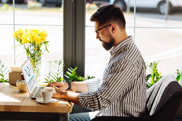 Concentré sur le travail. Bel homme sérieux tapant le texte tout en travaillant sur son ordinateur portable