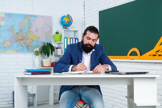 Concentré sur le travail étudiant assis dans la salle de classe pendant que la leçon réussit l'examen en apprenant le sujet homme sérieux avec barbe regarde les problèmes de cahier dans l'étude de l'éducation informelle