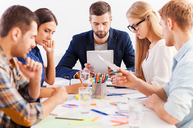 Concentré sur le travail. Groupe d'hommes d'affaires confiants dans des vêtements décontractés intelligents travaillant ensemble tout en étant assis à la table