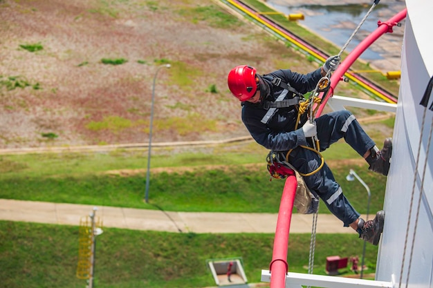 Concentrez l'inspection des travailleurs masculins portant la première ligne de sécurité de la corde du harnais de sécurité travaillant sur un toit de réservoir élevé sur le tuyau