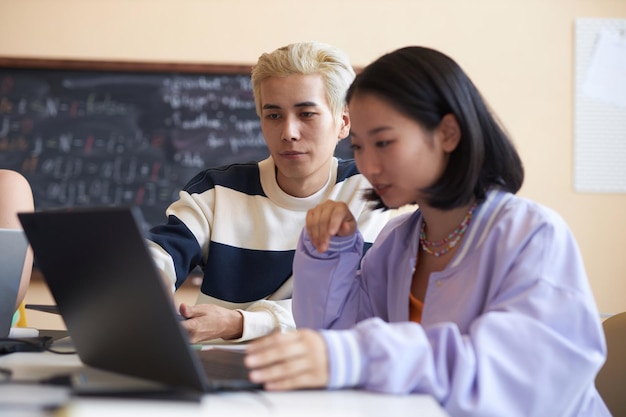 Photo concentrez-vous sur un jeune homme asiatique confiant faisant une présentation à une camarade de classe assis à côté d'elle et regardant tous les deux l'écran d'un ordinateur portable