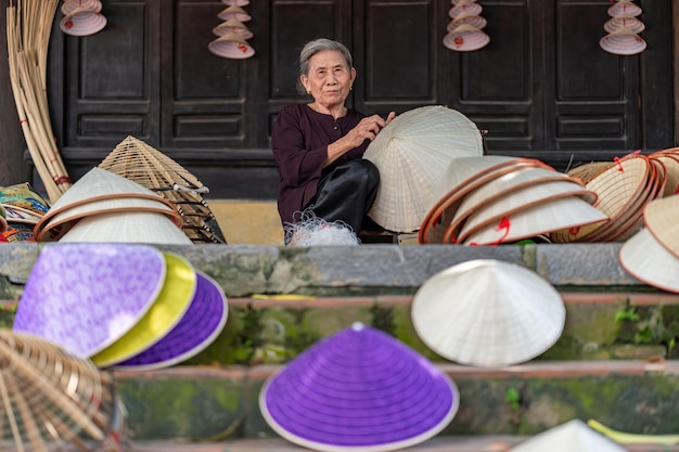 Photo concentrez-vous sur une vieille femme fabriquant des chapeaux coniques à la main devant le temple. le nom vietnamien est le village de non la lang chuong, la ville de hanoi, le concept de voyage au vietnam