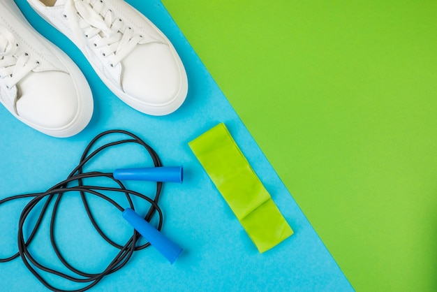 Concept d'accessoires de remise en forme Vue de dessus photo d'une corde à sauter avec bande élastique et baskets blanches sur fond vert bleu bicolore avec espace vide