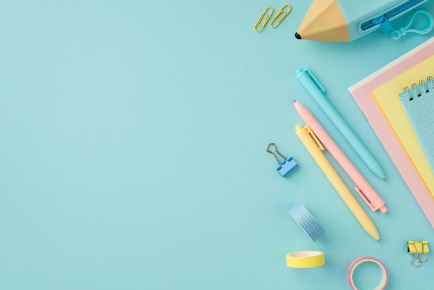 Concept d'accessoires scolaires Photo vue de dessus de cahiers de papeterie colorés étui à crayons ruban adhésif clips et stylos sur fond bleu pastel isolé avec espace de copie