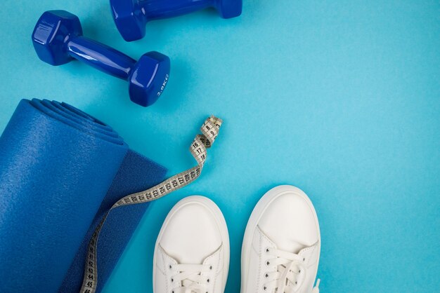 Le concept d'accessoires sportifs Photo de baskets blanches, d'haltères bleus et d'un tapis d'exercice bleu et d'autres équipements sportifs