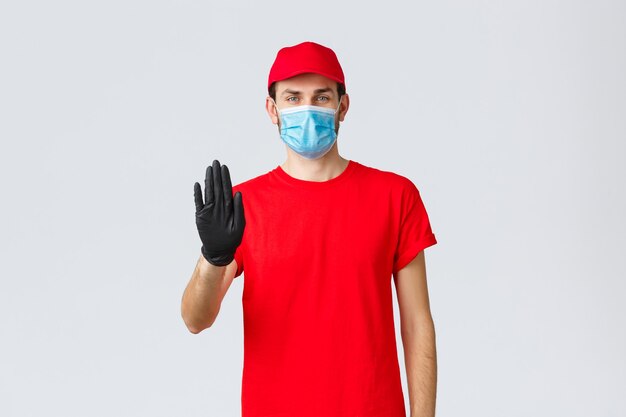 Concept d'achat en ligne d'auto-quarantaine Covid livreur confiant en gants d'uniforme rouges et visage m...