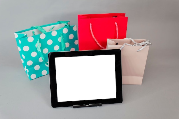 Concept d'achat en ligne. Maquette de tablette gros plan avec écran blanc avec des sacs-cadeaux lumineux sur fond gris.