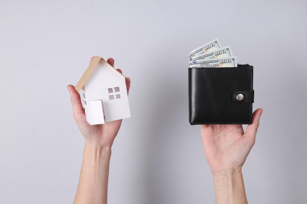 Concept d'achat de maison Les mains tiennent une mini maison et un sac à main sur fond gris