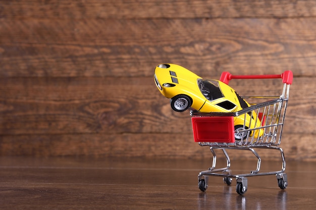 Concept d'achat d'une nouvelle voiture. Petite voiture dans le panier sur la table en bois