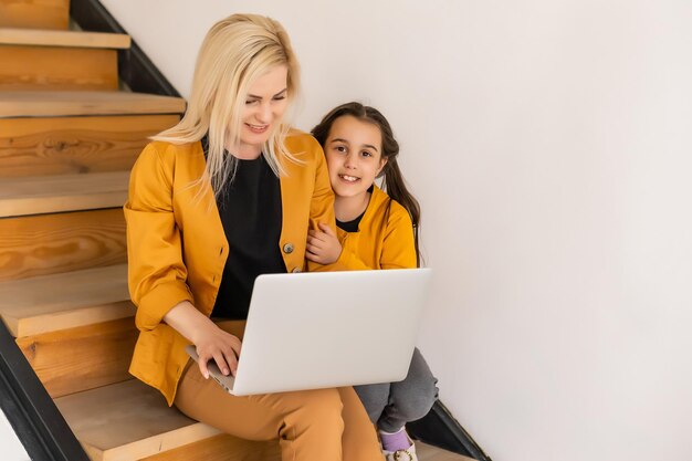 Concept d'achat ou de paiement en ligne. La mère enseigne à sa fille à l'aide d'un ordinateur portable à la maison. Assis sur les marches de l'escalier.