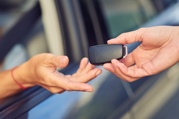 Concept d'achat de voiture gros plan d'une main masculine donnant des clés de voiture à une femme assise derrière