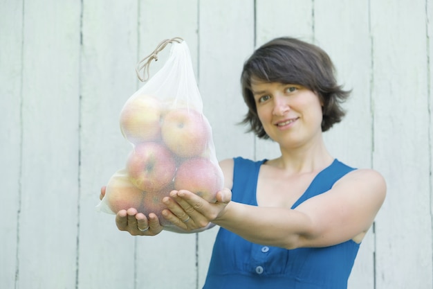 Photo concept d'achat zéro déchet. pas de plastique à usage unique. femme souriante tenant un sac de produits réutilisables en maille recyclée avec des pommes biologiques fraîches