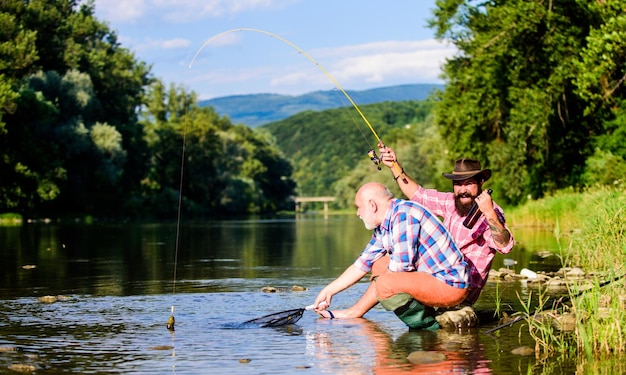 Concept d'activité de pêche papa à la retraite et fils barbu mature pêche au gros pêcheur heureux amitié deux amis masculins pêchant ensemble poisson à la mouche passe-temps des hommes pêche à la retraite