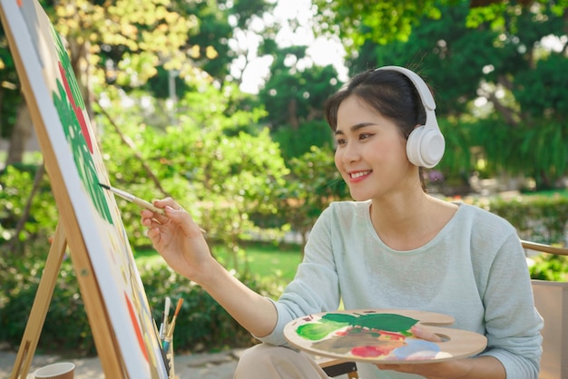 Concept d'activité de plein air Artiste féminine écoutant de la musique tout en peignant une image sur toile dans le jardin