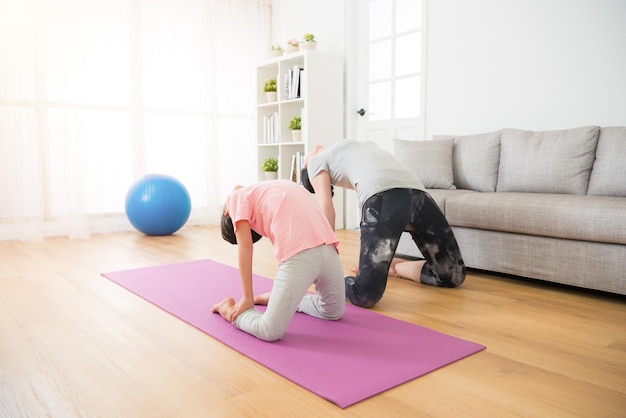 concept d'activités familiales d'exercice de yoga sportif. enfant et mère s'entraînent à la douceur du corps dans le salon en faisant sur le parquet près d'un canapé confortable.