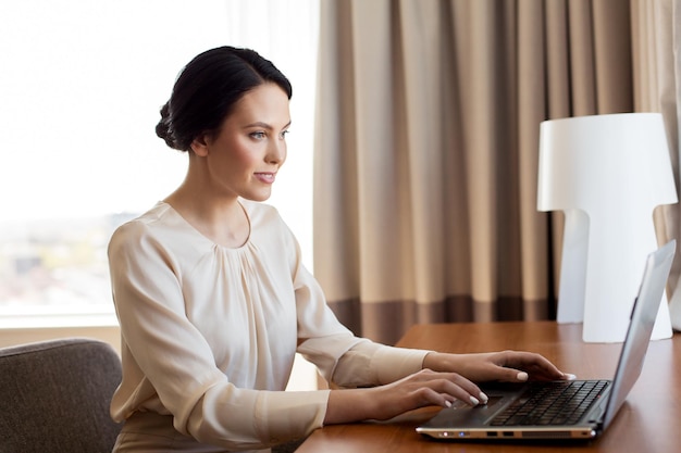 concept d'affaires, de personnes et de technologie - femme d'affaires tapant sur un ordinateur portable dans une chambre d'hôtel