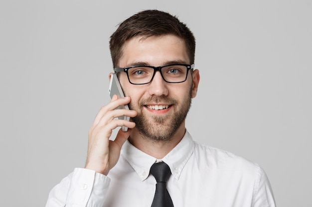 Concept d&#39;affaires - Portrait jeune homme d&#39;affaire joyeux beau en costume parler au téléphone en regardant la caméra. Fond blanc. Espace de copie.