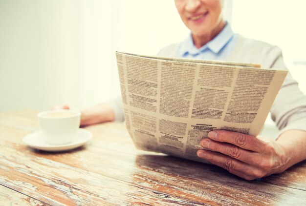 concept d'âge, de loisirs et de personnes - gros plan d'une femme âgée heureuse buvant du café et lisant un journal à la maison