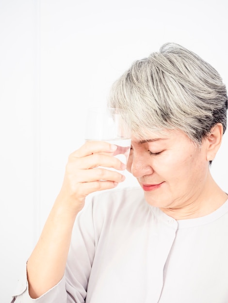 Concept d'âge, de soins de santé et de personnes - femme asiatique âgée heureuse avec un verre d'eau à la maison