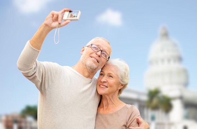 concept d'âge, de tourisme, de voyage, de technologie et de personnes - couple de personnes âgées avec caméra prenant selfie dans la rue sur fond de maison blanche de washington