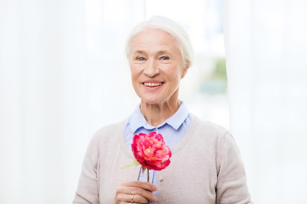concept d'âge, de vacances et de personnes - femme senior souriante heureuse avec fleur à la maison