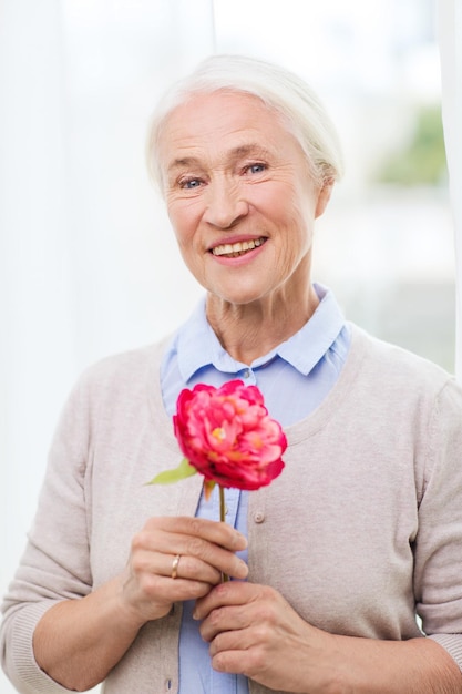 concept d'âge, de vacances et de personnes - femme senior souriante heureuse avec fleur à la maison