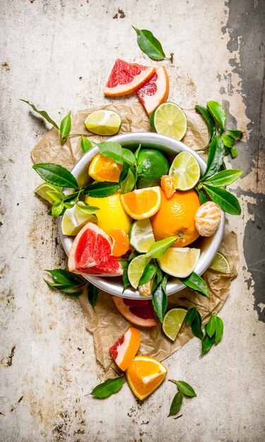 Le concept d'agrumes - pamplemousse, orange, mandarine, citron, citron vert dans un bol avec des feuilles