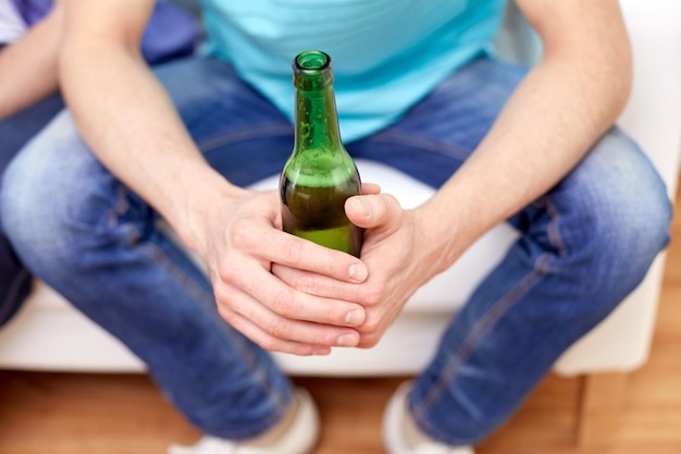concept d'alcool et de personnes - hommes avec des bouteilles de bière assis sur un canapé à la maison