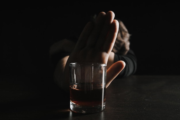 Concept d'alcoolisme L'homme pousse le verre de boisson alcoolisée avec du whisky assis seul la nuit