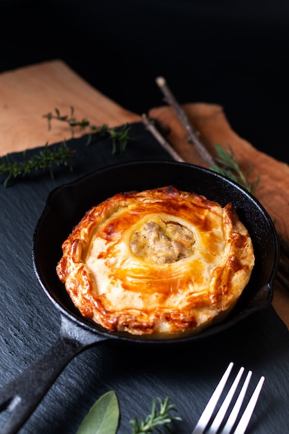 Concept alimentaire fait maison tarte feuilletée à la viande dorée dans une poêle en fonte sur une ardoise noire avec copie espace