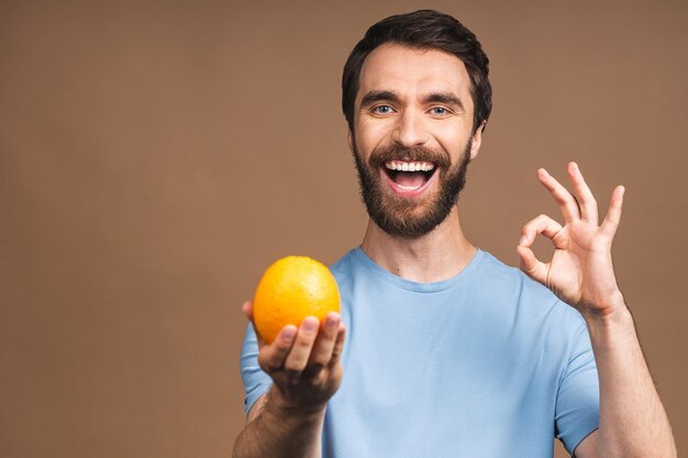 Concept d'alimentation et d'alimentation saine. Portrait de jeune homme souriant barbu tenant un fruit orange isolé sur fond beige.