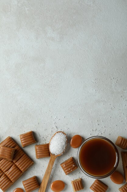 Concept d'aliments sucrés avec des morceaux de caramel, sel et sauce caramel sur fond texturé blanc