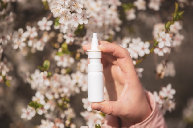 Concept d'allergie, jeune femme avec nez ou spray nasal à la main devant la floraison d'un arbre au printemps, soins de santé