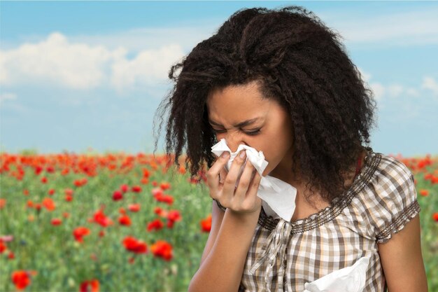 Concept d'allergies ou de froid. Jeune femme se moucher sur fond de champ de coquelicots