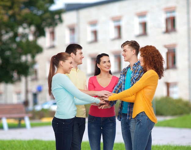 Concept d'amitié, d'éducation, de travail d'équipe, de geste et de personnes - groupe d'adolescents souriants se mettant la main les uns sur les autres sur fond de campus