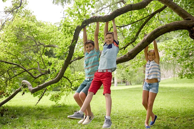 concept d'amitié, d'enfance, de loisirs et de personnes - groupe d'enfants ou d'amis heureux accrochés à l'arbre et s'amusant dans le parc d'été
